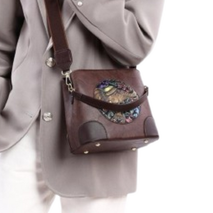 Brown leather handbag with decorative element worn over a gray coat