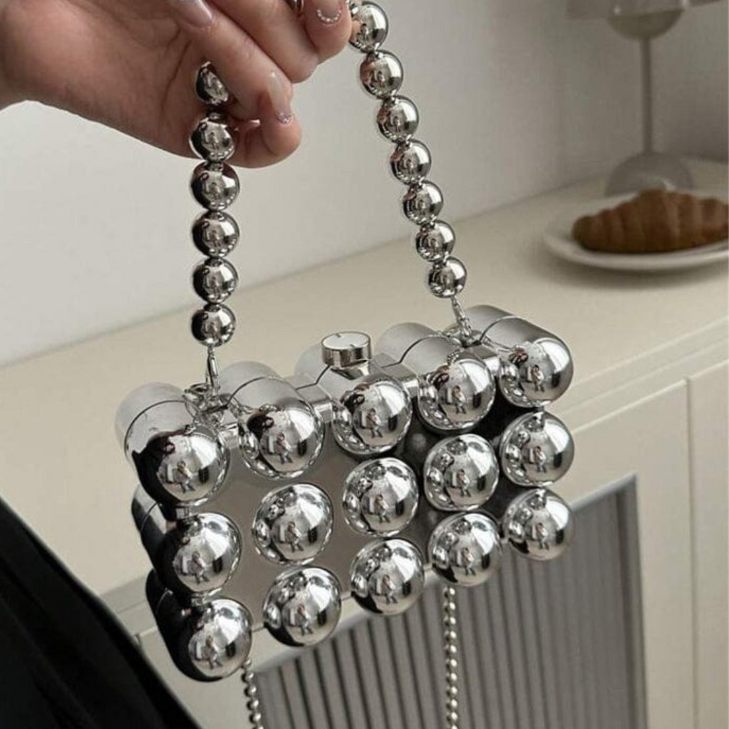 Silver beaded handbag held by a hand on a neutral background